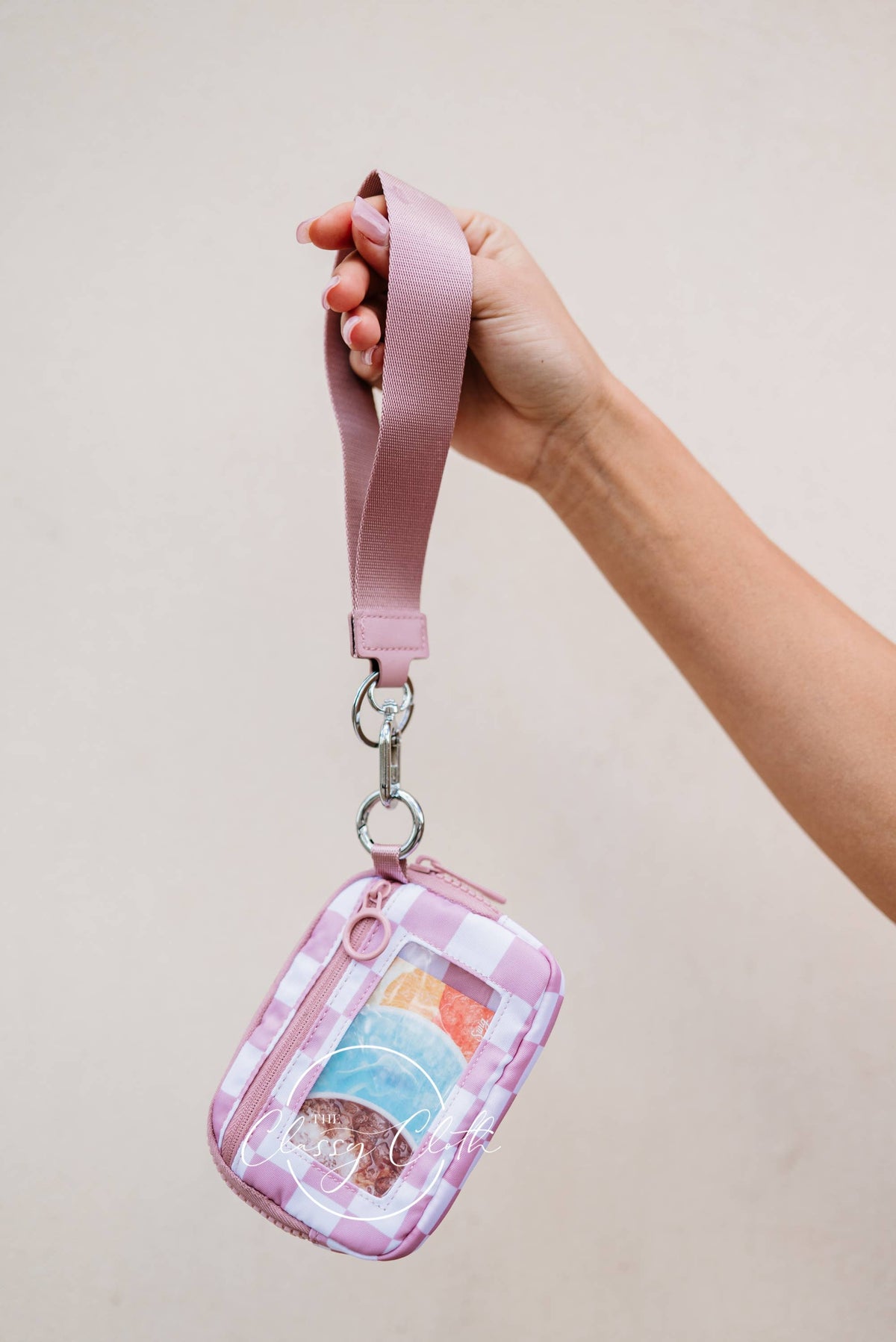 Hand holding a pink lanyard with a small pouch featuring colorful designs against a plain background