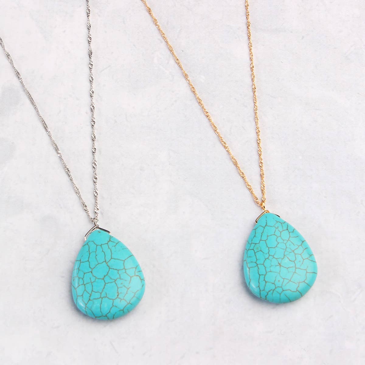 Two turquoise teardrop pendants on gold and silver chains against a white background