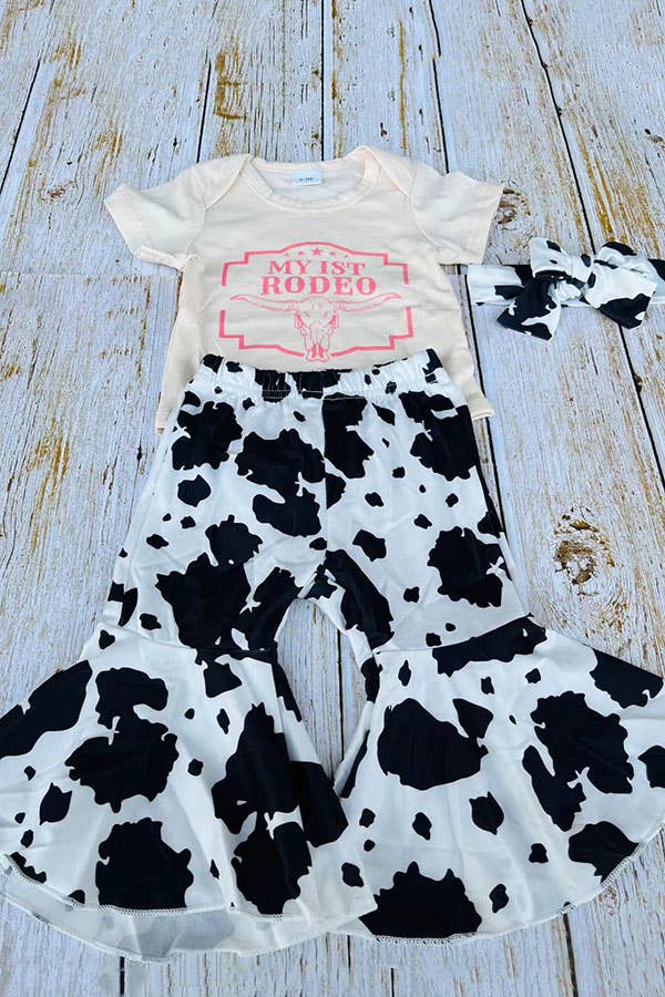 Baby outfit with cow print pants and 'My 1st Rodeo' shirt on a wooden surface