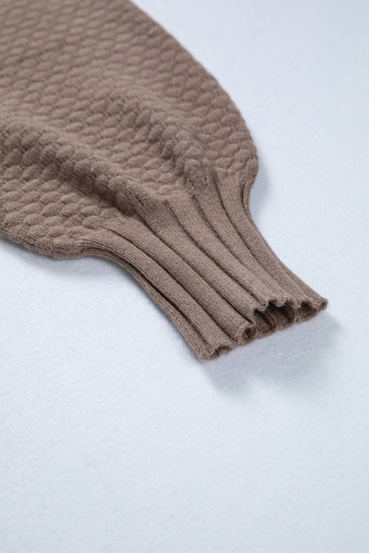 Close-up of a brown knitted sweater sleeve on a light gray background