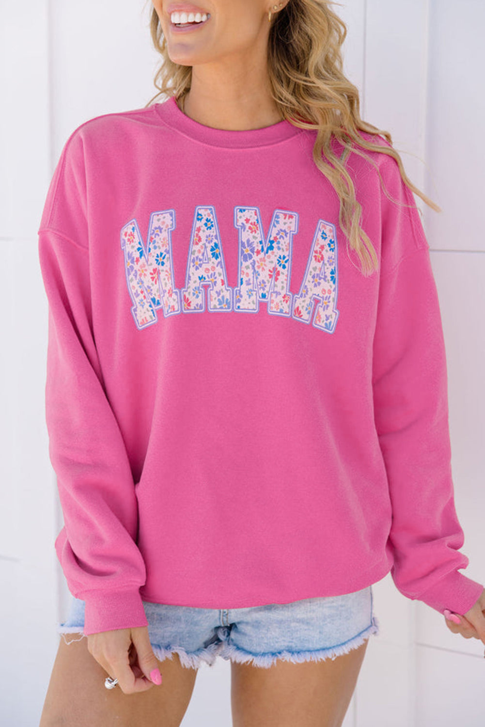 Person wearing a pink sweatshirt with floral 'MAMA' text against a white background