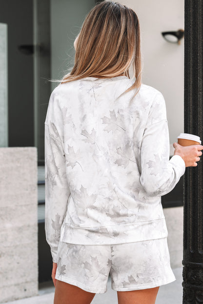Woman wearing a light gray floral sweatshirt and shorts set, holding a coffee cup.