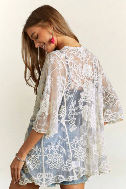 Woman wearing a white lace kimono over a blue dress against a plain background