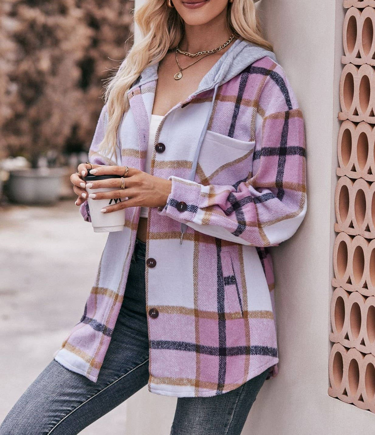 Woman wearing a pink plaid jacket holding a coffee cup against a decorative wall.