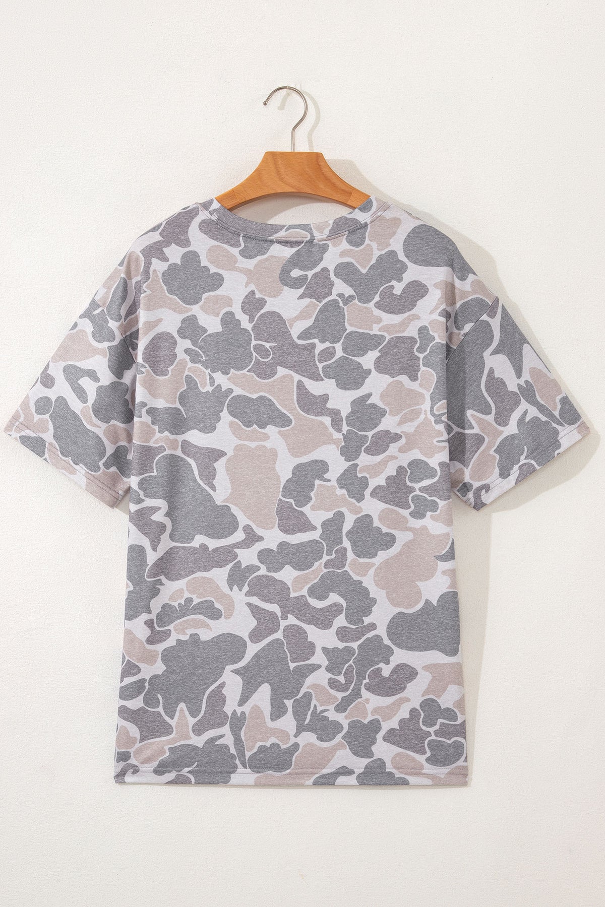 Camouflage-patterned t-shirt on a wooden hanger against a white background