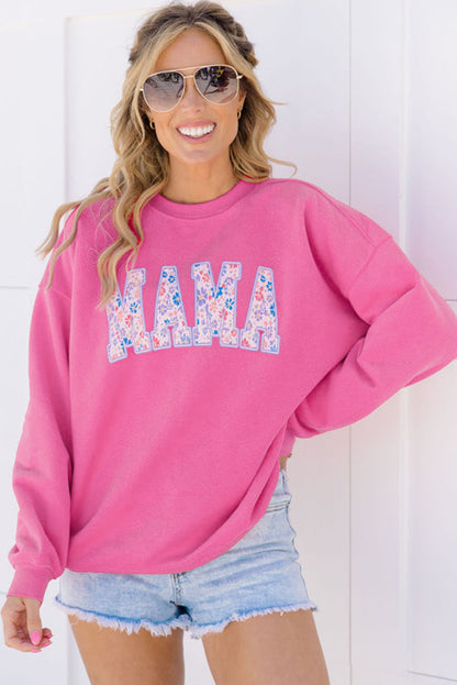 Woman wearing a pink sweatshirt with floral 'MAMA' text and denim shorts against a white background