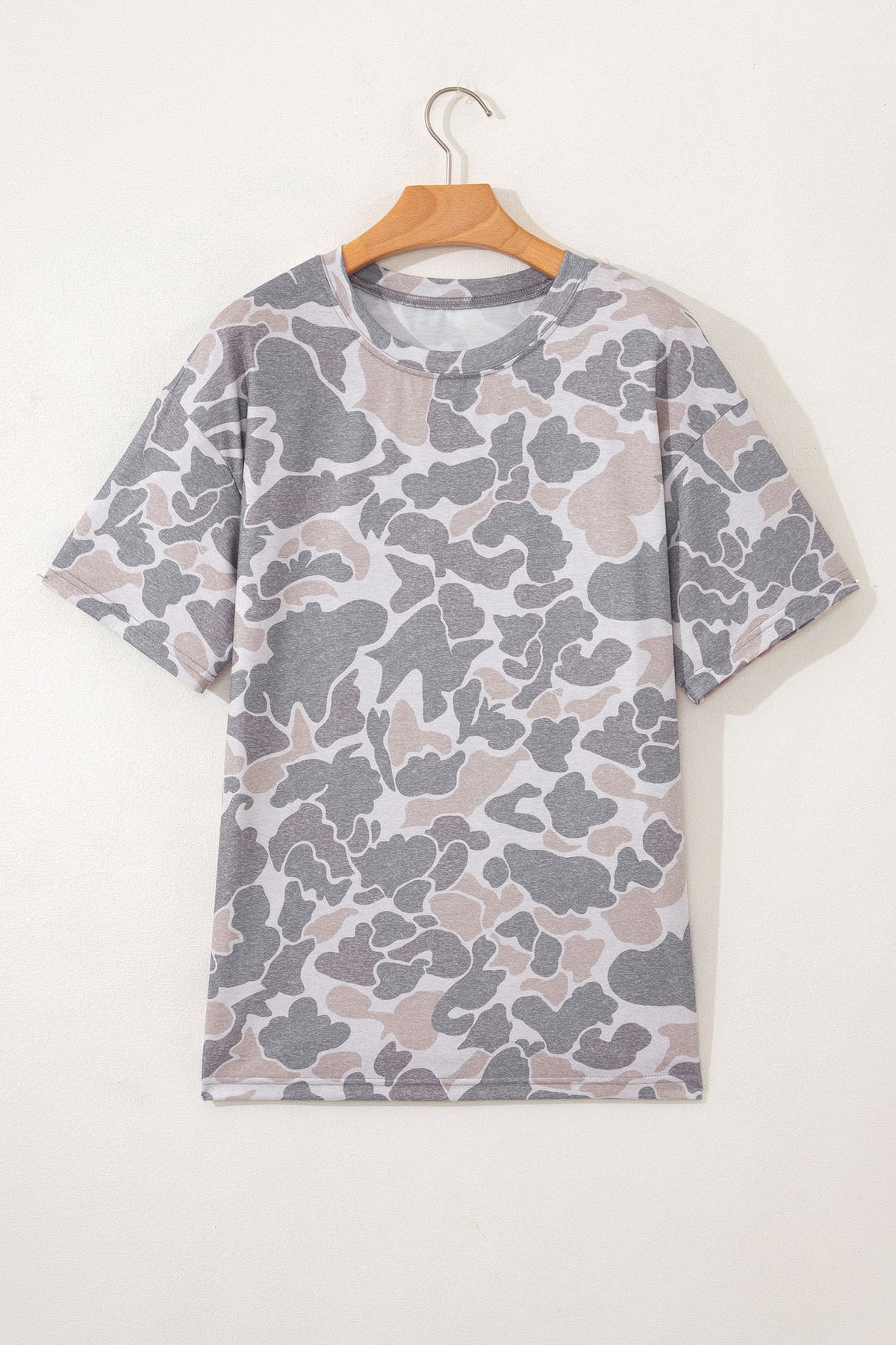 Camouflage-patterned t-shirt on a wooden hanger against a white background