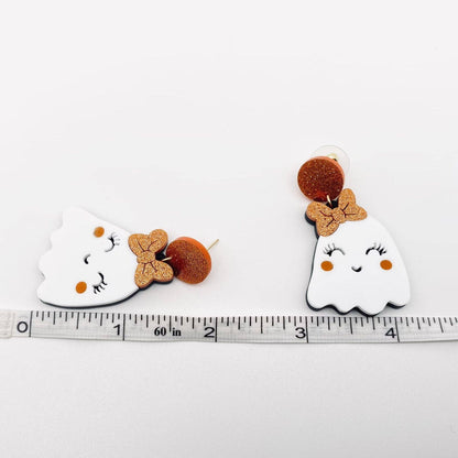 Pair of ghost-shaped earrings with bow details on a ruler for scale.
