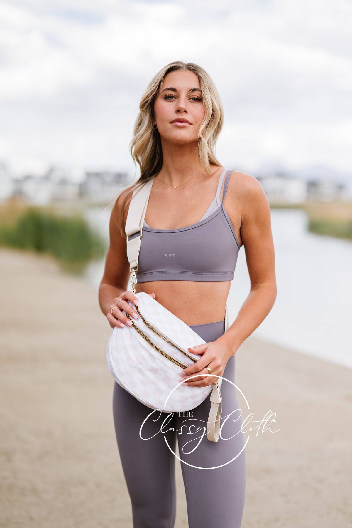 Woman in athletic wear holding a white bag on a beach with 'Classic Cloth' branding.