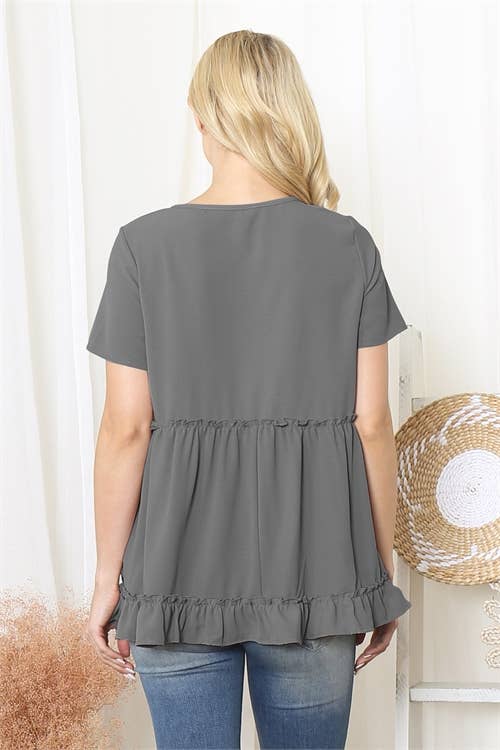 Woman wearing a gray ruffled blouse with a white curtain background