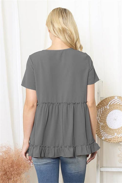 Woman wearing a gray ruffled blouse with a white curtain background