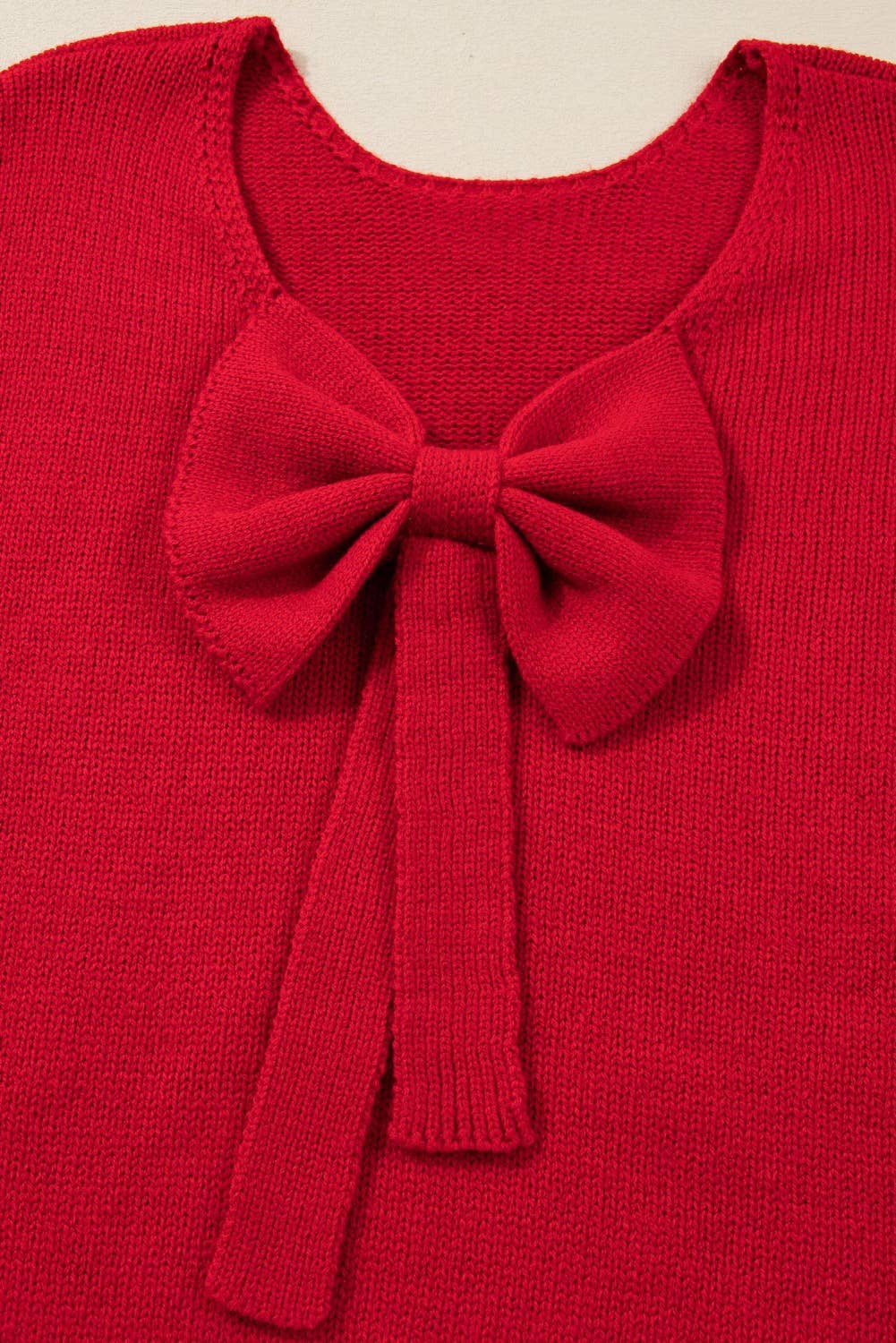 Red sweater with a large bow detail on a beige background