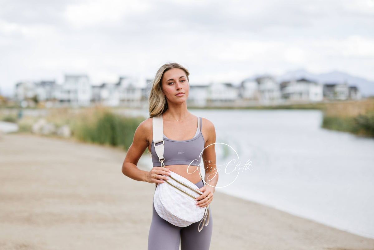 Woman in athletic wear standing by a waterfront with a white bag.