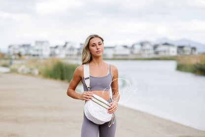 Woman in athletic wear standing by a waterfront with a white bag.
