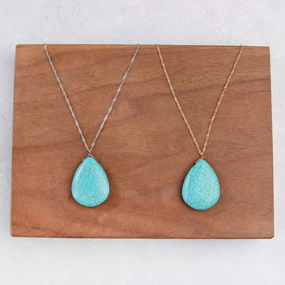 Two turquoise teardrop pendants on gold and silver chains against a wooden background.