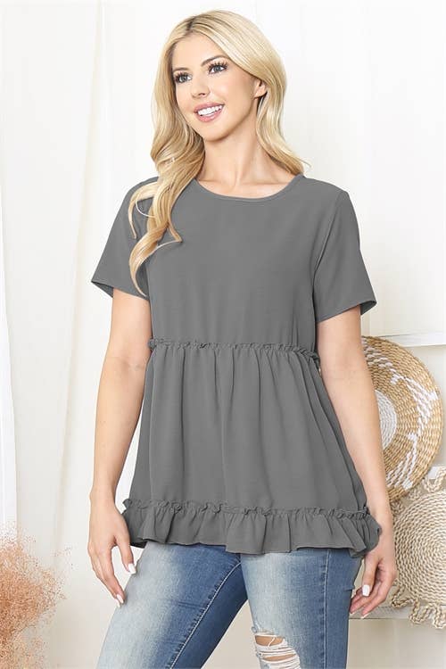 Woman wearing a gray peplum top and blue jeans against a white background