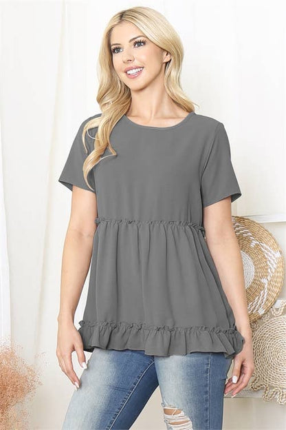Woman wearing a gray peplum top and blue jeans against a white background