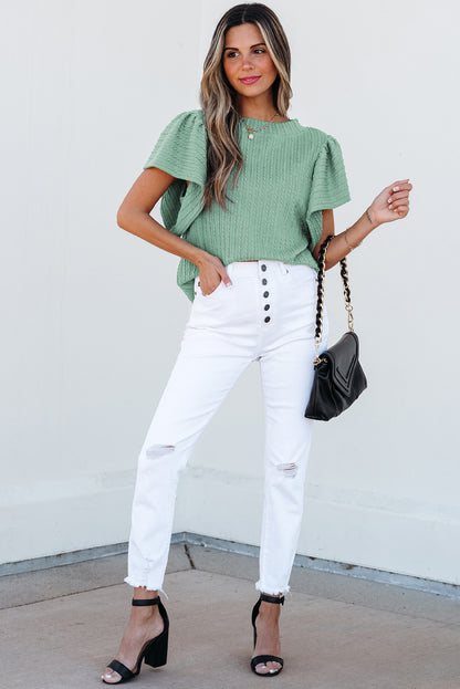 Woman wearing a green top and white pants with a black handbag against a white background