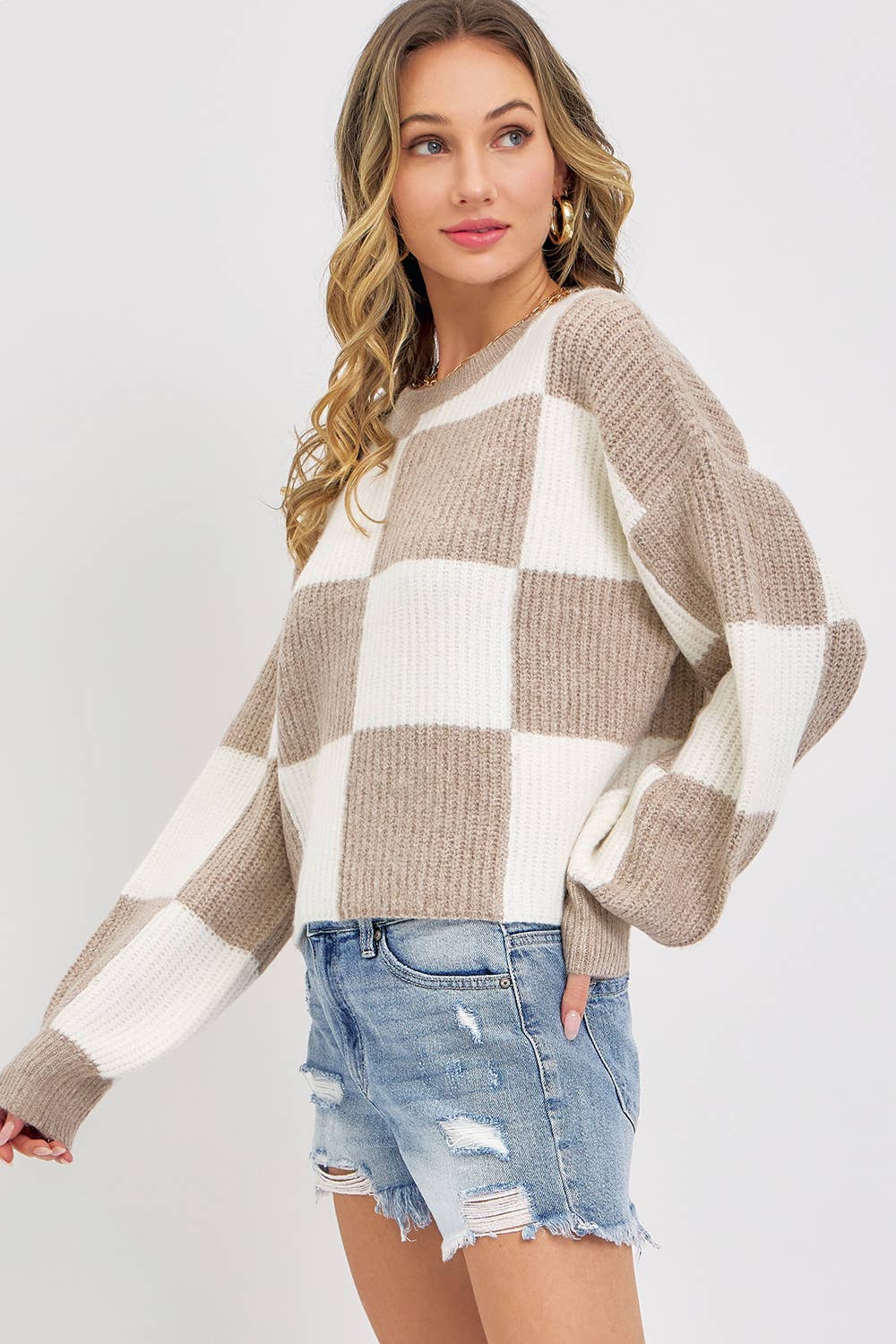 Woman wearing a checkered sweater and denim shorts on a plain background