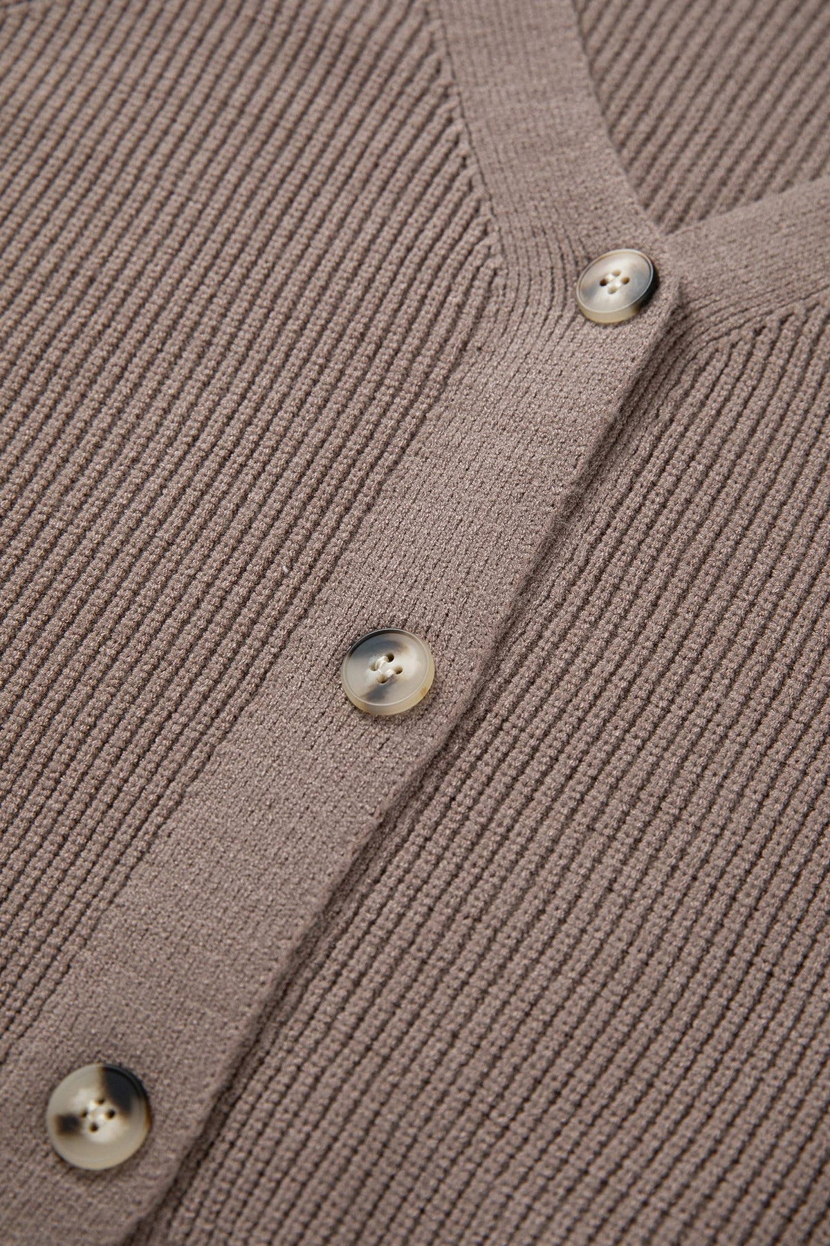 Close-up of a ribbed knit cardigan with buttons on a brown background
