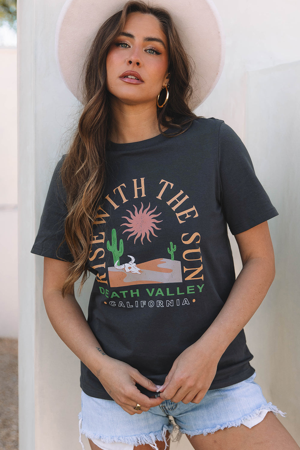 Woman wearing a black t-shirt with a graphic design and text, standing against a white wall.
