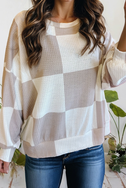 Person wearing a checkered sweater with a neutral color palette, standing indoors.