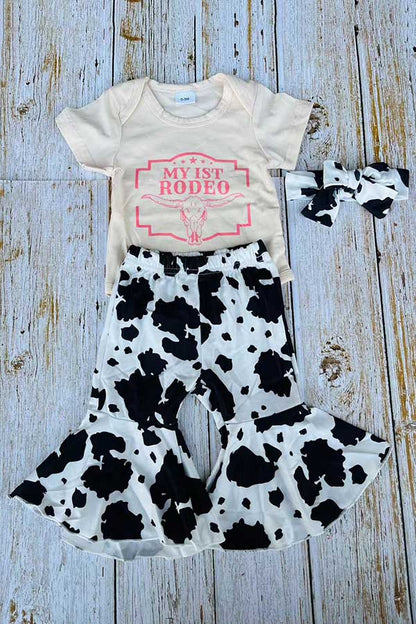 Baby outfit with cow print pants and 'My 1st Rodeo' shirt on a wooden surface