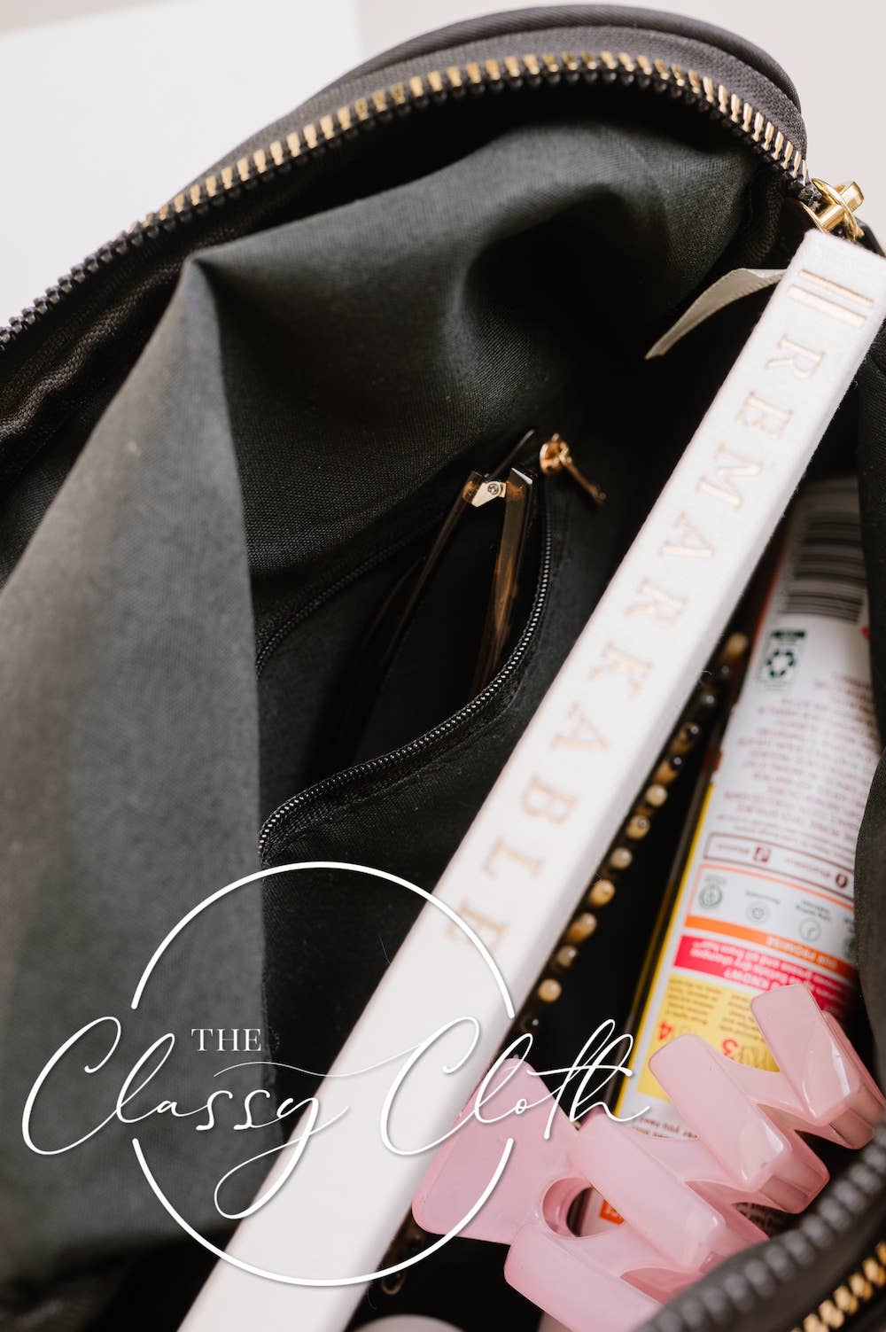 Black bag with a white handle and pink item inside, featuring 'The Classy Cloth' logo.