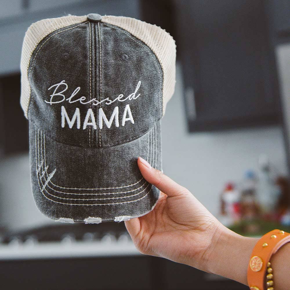 Black denim cap with 'Blessed Mama' text held by a hand in a kitchen setting