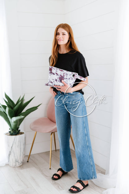 Woman holding a clutch in a minimalistic room with a plant and chair.
