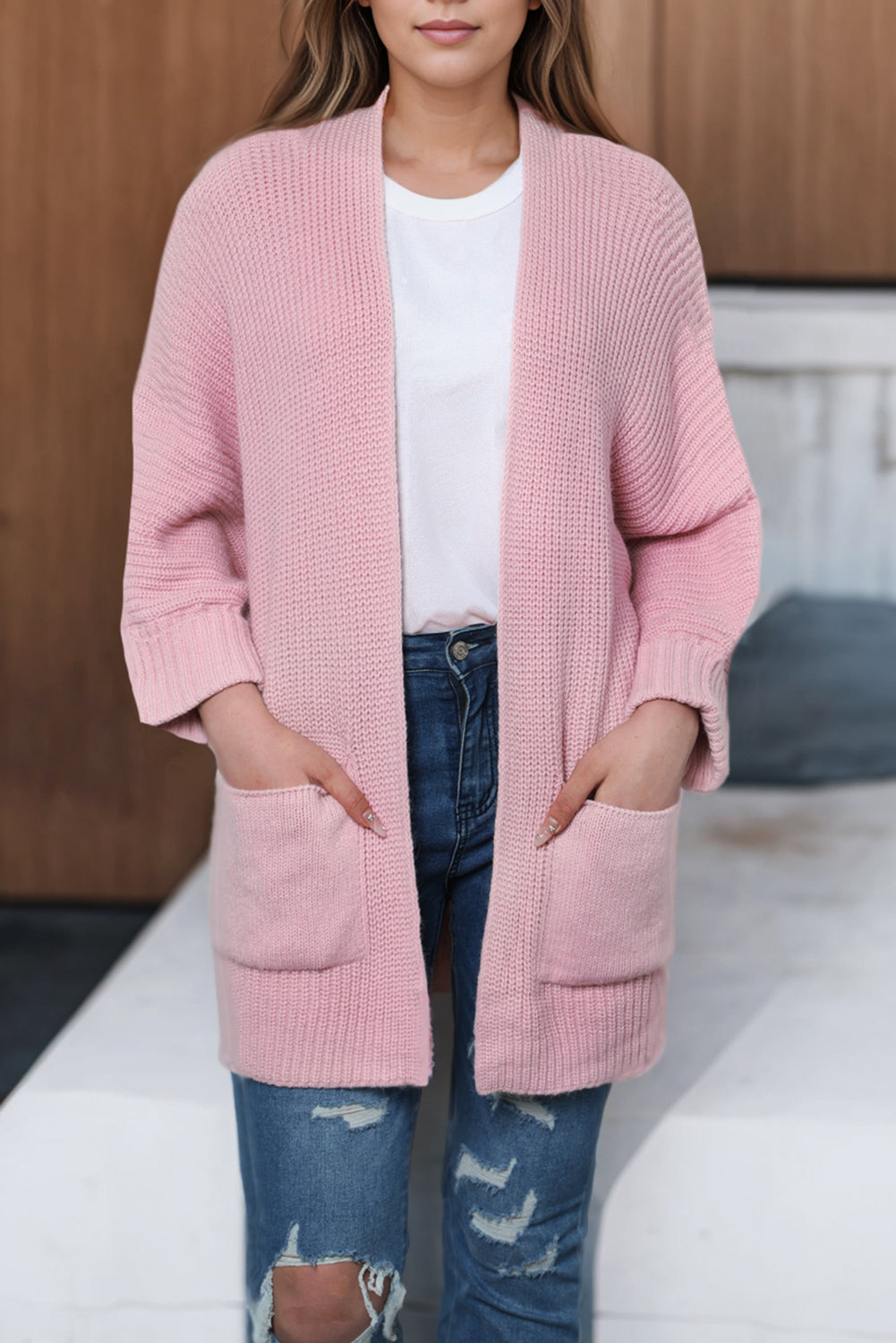 Person wearing a pink cardigan over a white shirt and blue jeans on a neutral background