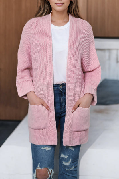 Person wearing a pink cardigan over a white shirt and blue jeans on a neutral background