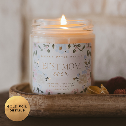 Candle in a jar labeled 'Best Mom Ever' with floral design and gold foil details, placed on a wooden tray.