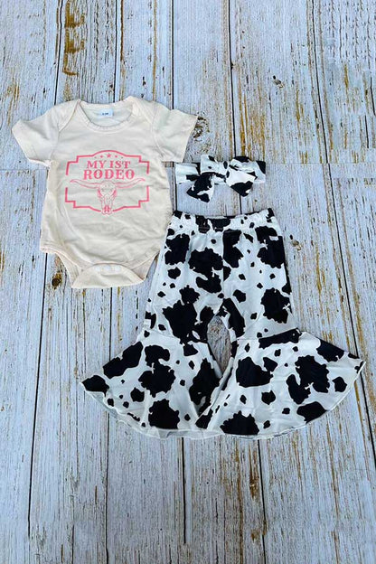 Baby outfit with white onesie and cow print romper on a wooden surface