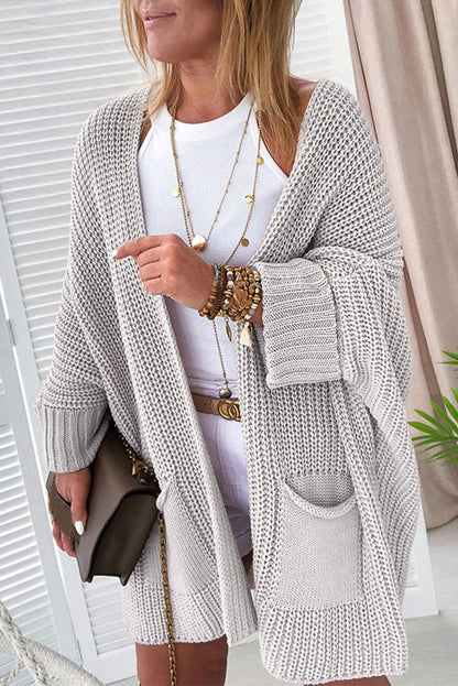 Woman wearing a long, light gray cardigan over a white top, holding a brown handbag.