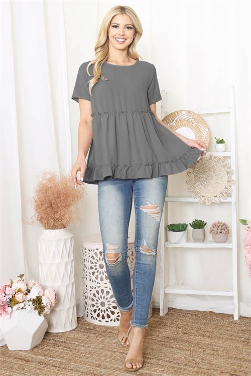 Woman wearing a gray peplum top and ripped jeans in a home setting.