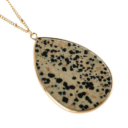 Teardrop-shaped pendant with dalmatian jasper stone on a gold chain against a white background