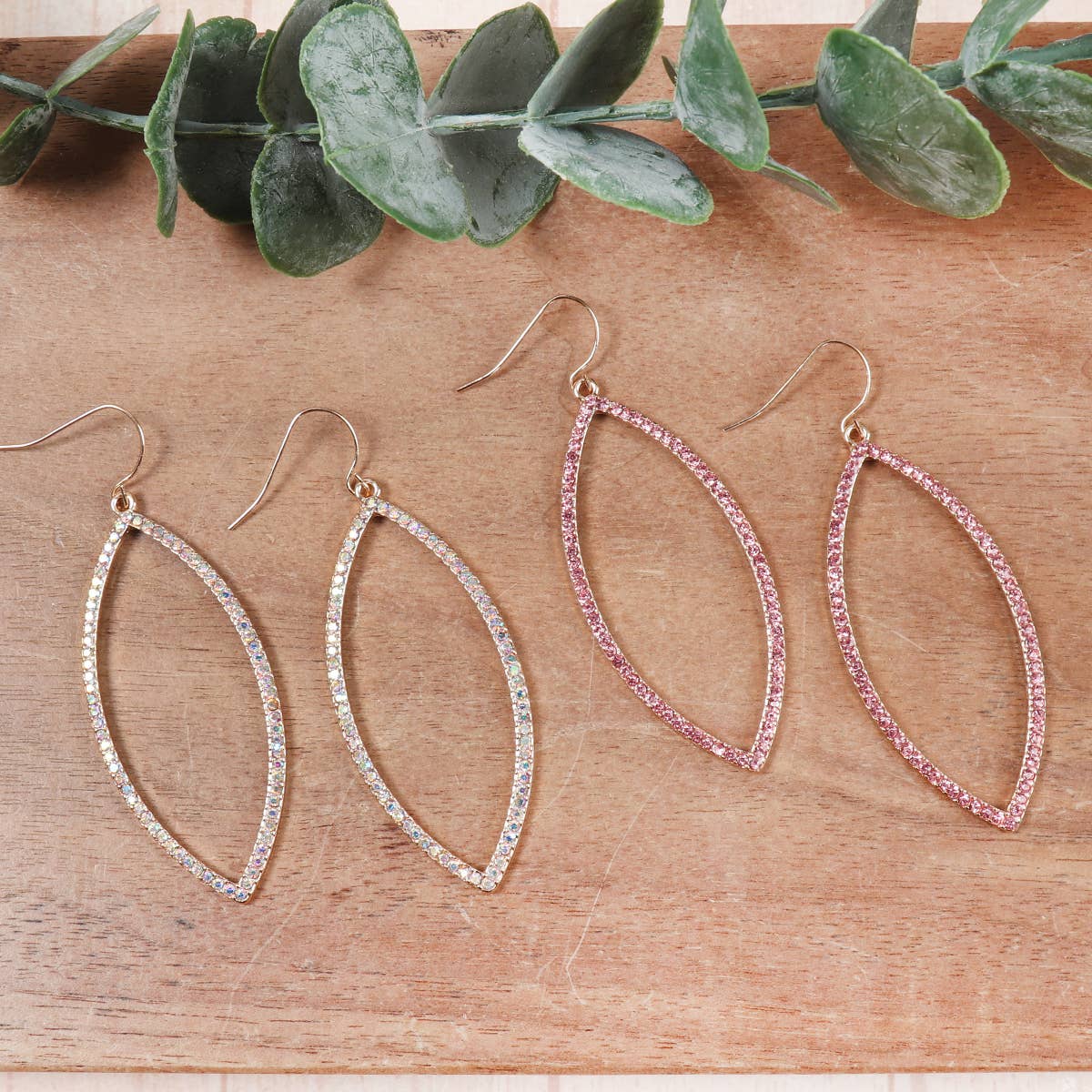 Two pairs of hoop earrings on a wooden surface with green leaves.