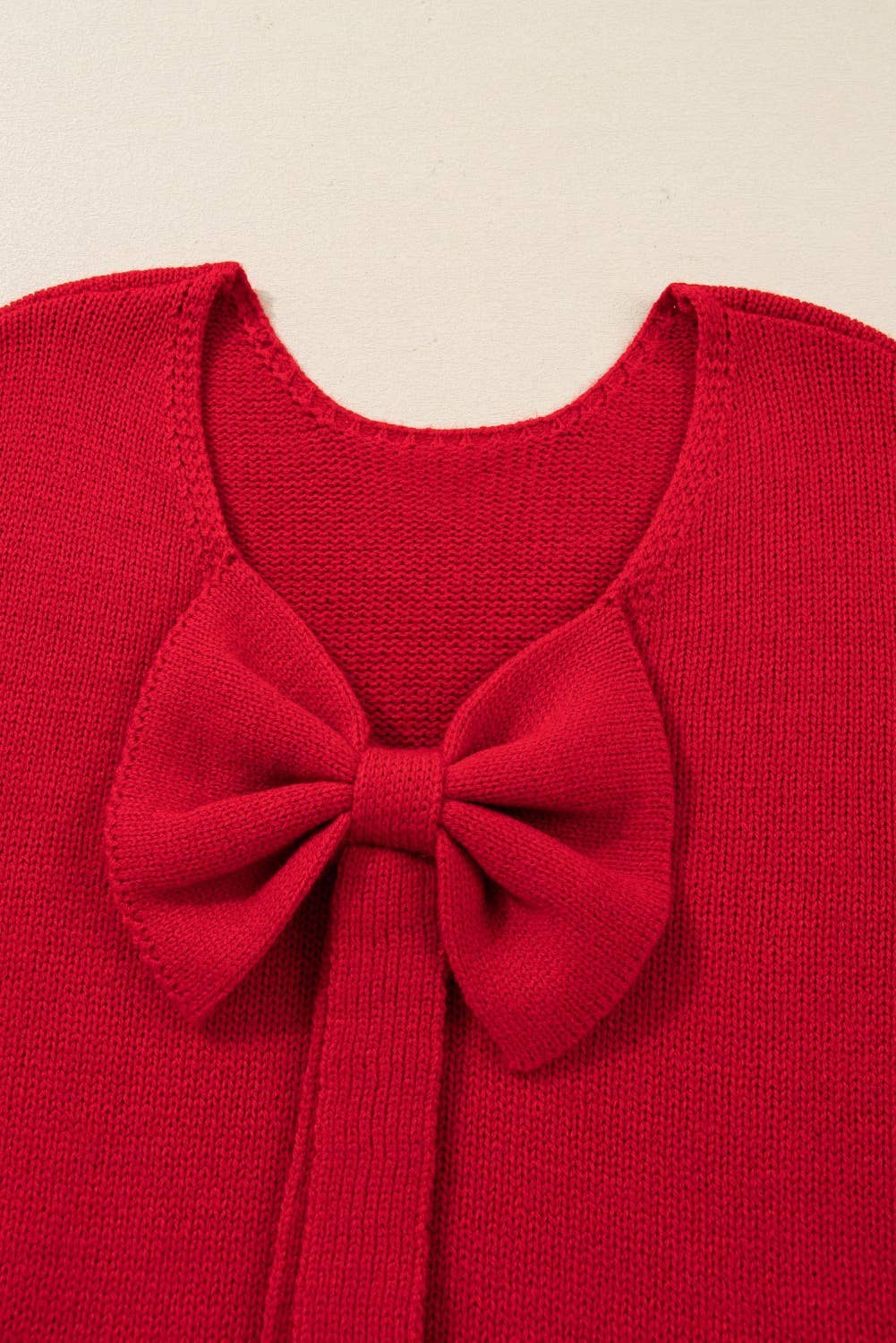 Red sweater with a large bow detail on a beige background