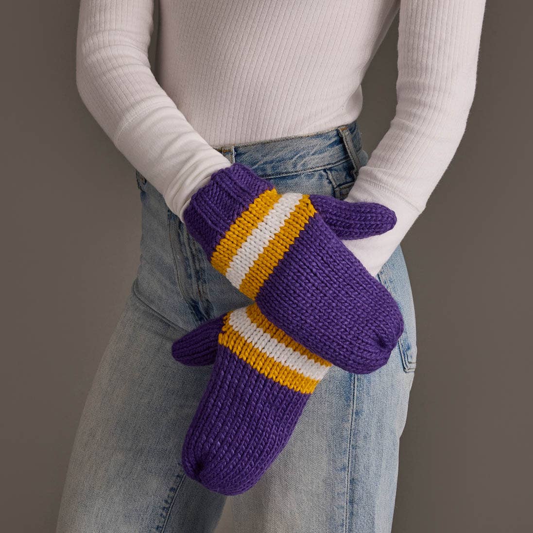 Purple, gold and white striped knit mittens worn with a white sweater and jeans