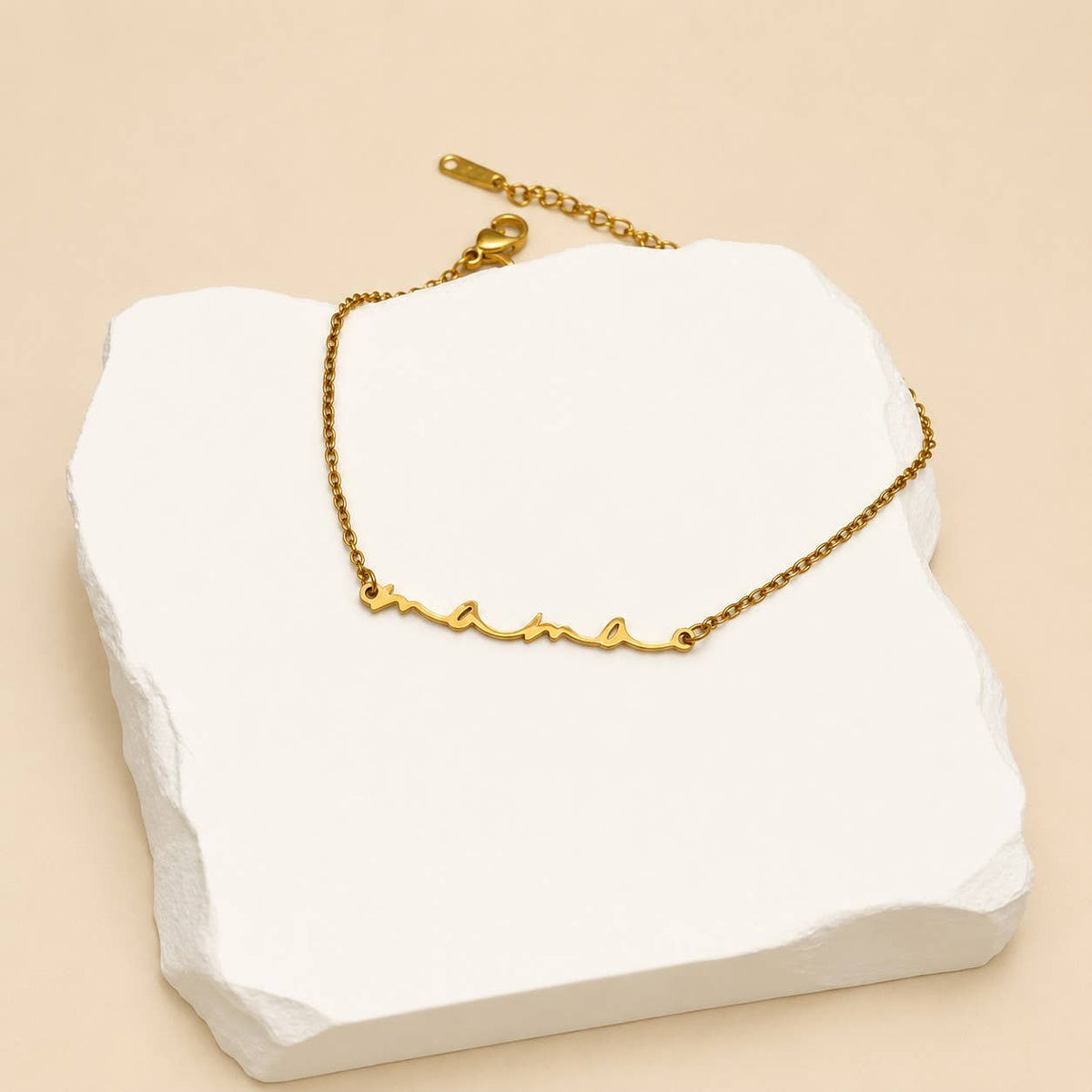 Dainty gold Mama script bracelet displayed on a white jewelry stand
