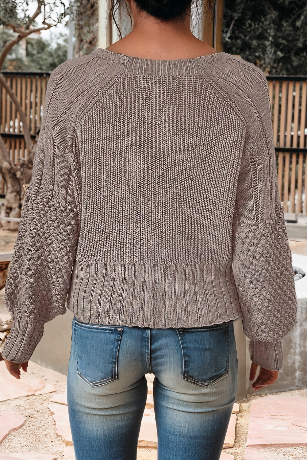 Person wearing a beige knitted sweater and blue jeans outdoors.