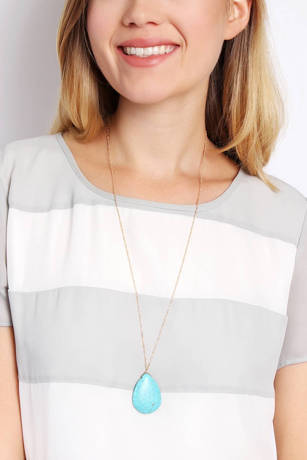 Woman wearing a necklace with a blue pendant against a neutral background