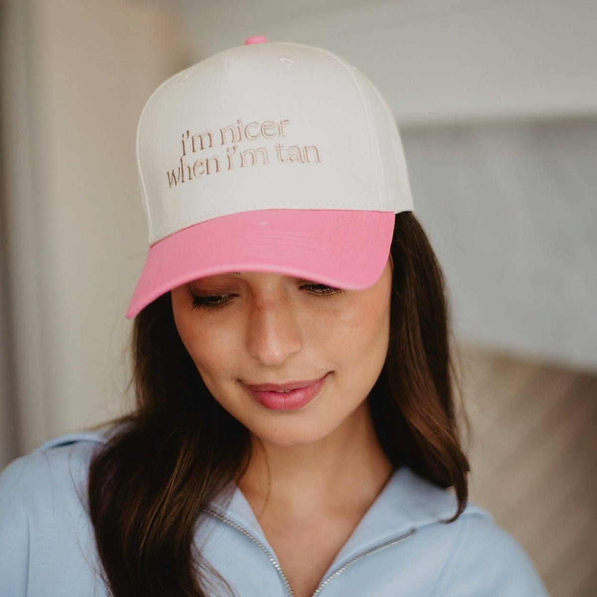 Person wearing a pink and beige cap with text, indoors.