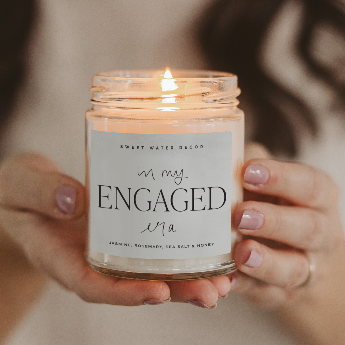 Candle labeled 'in my ENGAGED wa' held by a person with a blurred background