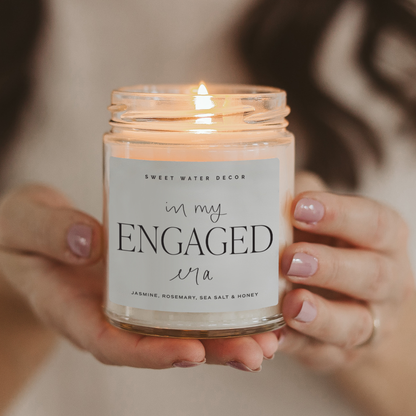 Candle labeled 'in my ENGAGED wa' held by a person with a blurred background