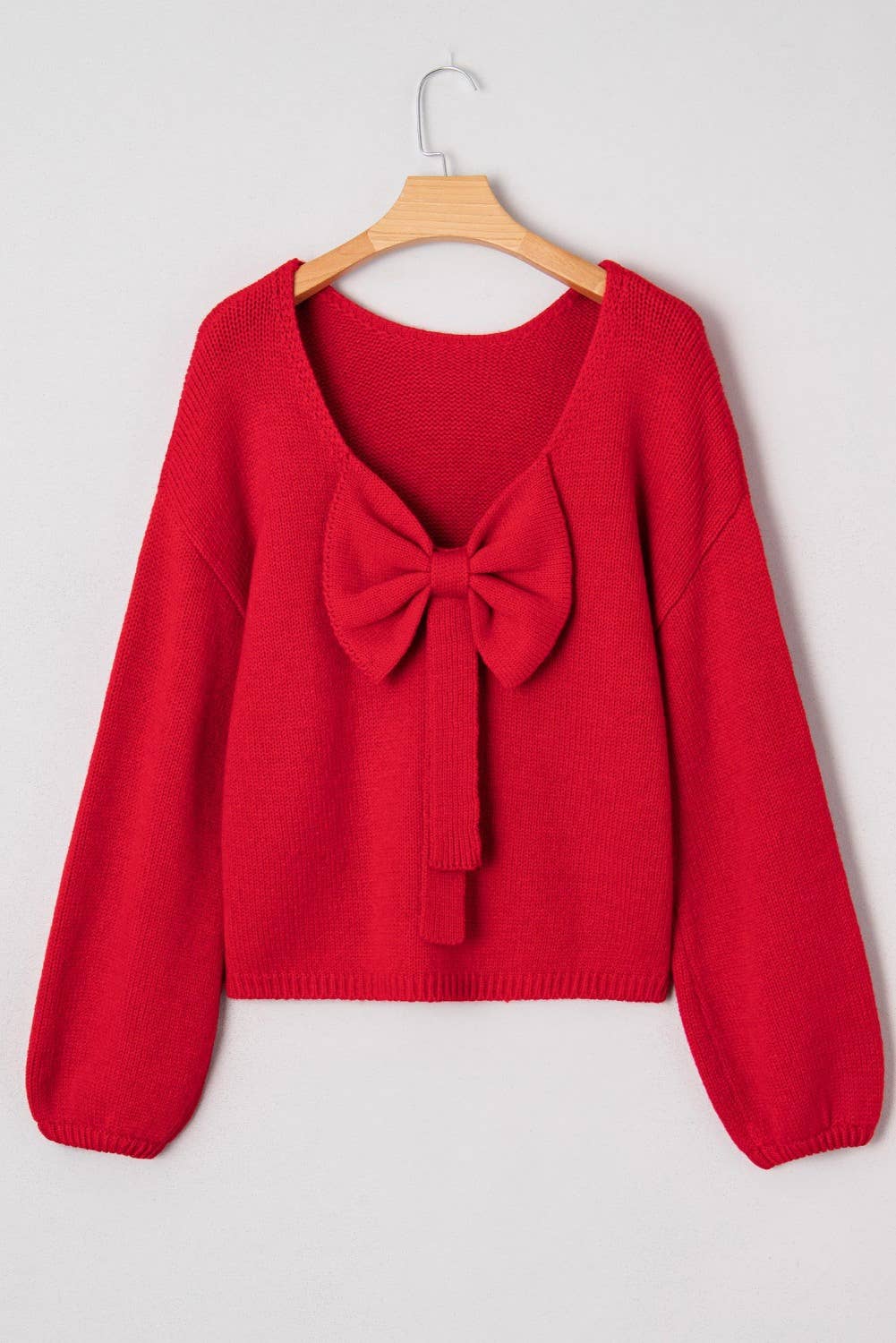 Red sweater with a large bow on a hanger against a white background