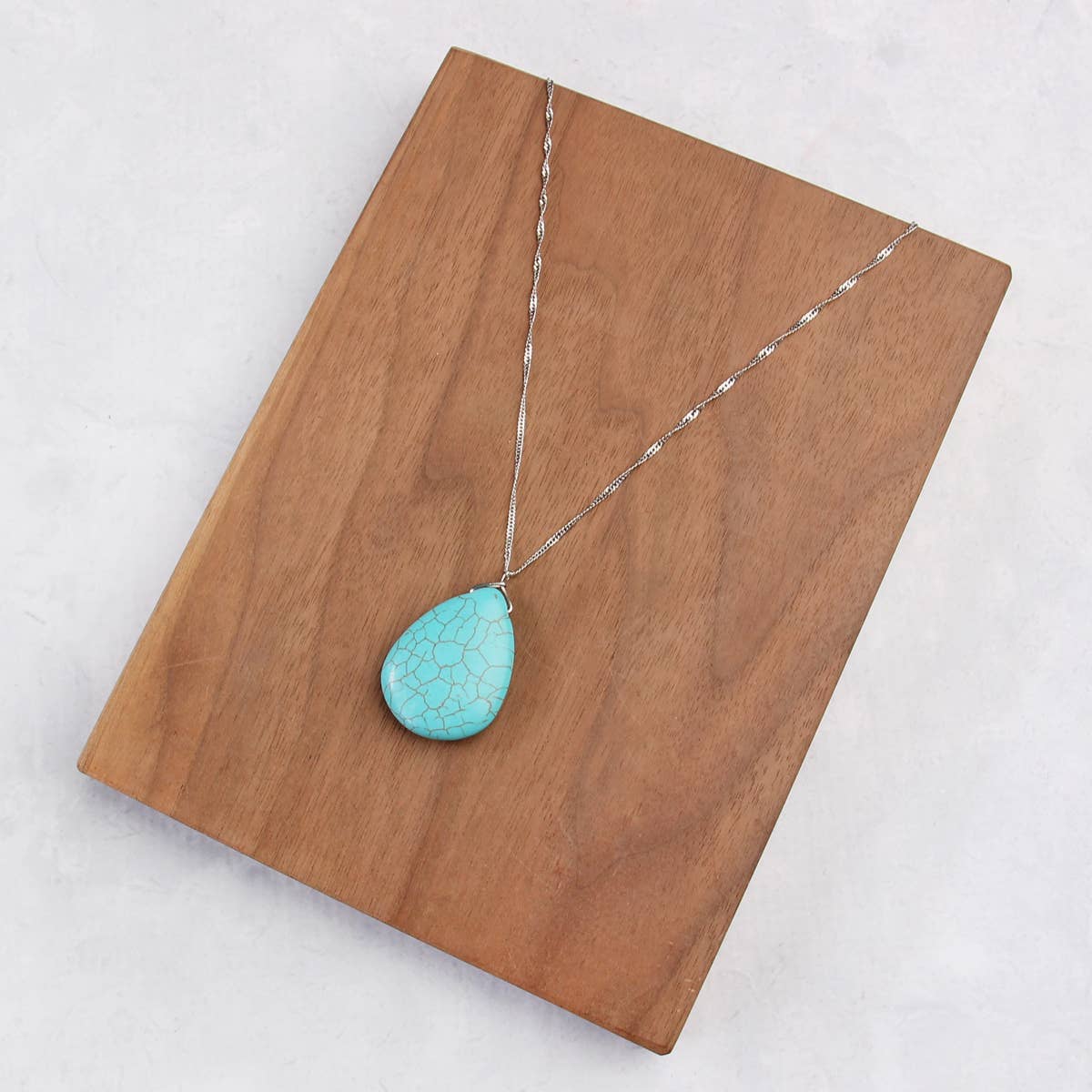 Turquoise pendant necklace on a wooden board with a white background