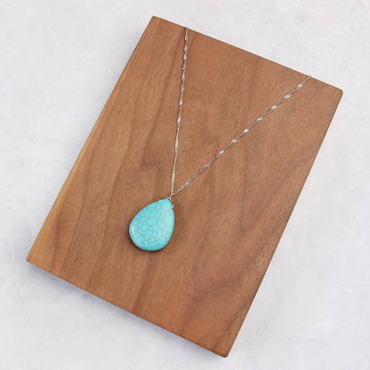 Turquoise pendant necklace on a wooden board with a white background