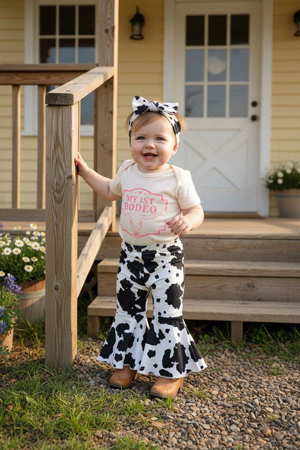 Baby girl wearing My First Rodeo western outfit with cow print bell bottom pants and matching headband